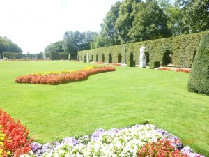 Перед дворцом вереница статуй, резные изгороди дугообразной формы и большой водоем украшают великолепные сады